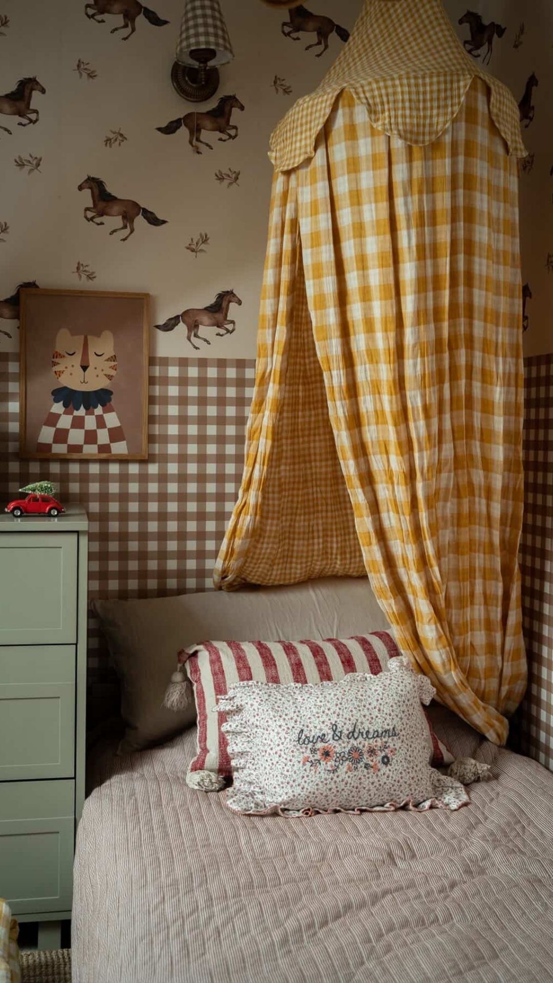 Aranżacja pokoju z baldachimem w żółtą kratkę, tapetą w konie i narzutą w paski.